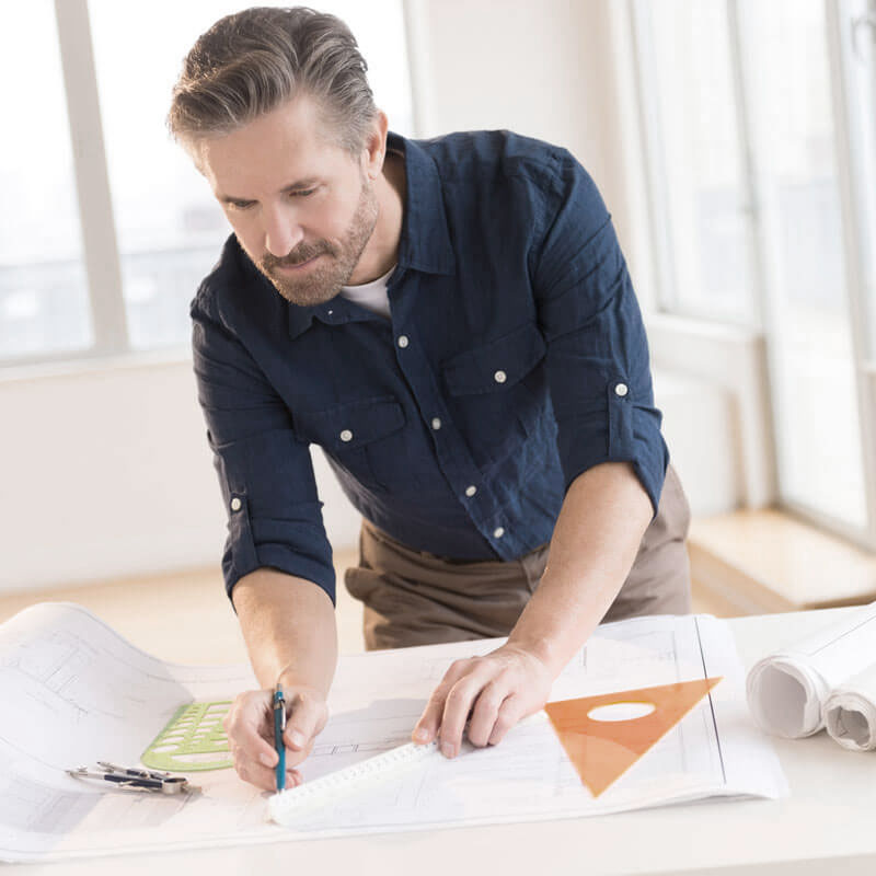 A caucasian man in his forties hunched over a drafting table, working on blueprints.